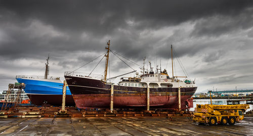 Sailboats moored at harbor against cloudy sky