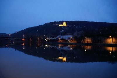 Illuminated city by lake against clear sky at night