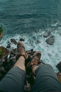 Low section of man sitting on mountain at sea