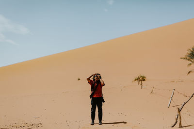Full length of man photographing while standing on sand in desert against sky