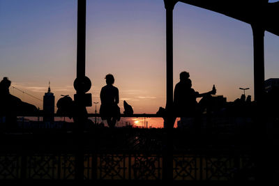 Silhouette of people sitting on railing at dusk