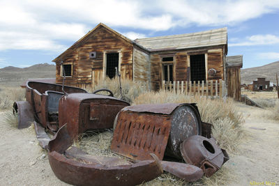 Abandoned rusty metal by barn on field against sky