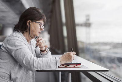 Side view of senior businesswoman using hands-free device by window in office