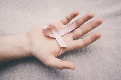 Cropped hand of man holding breast cancer awareness ribbon over bed