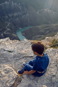 Boy child in a blue linen jumpsuit sit on the cliff of the sulak canyon in dagestan