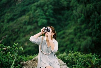 Woman photographing while sitting on rock