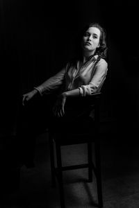 Young woman sitting on chair against black background