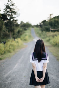 Rear view of woman standing on road against trees