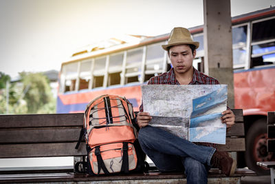 Male tourist holding map while sitting on bench in city