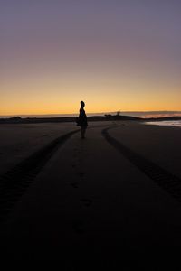 Silhouette man standing on beach against sky during sunset