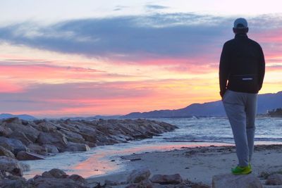 Rear view of man standing at beach during sunset