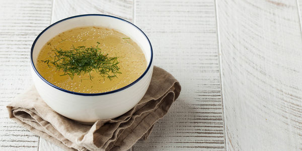 Healthy bone broth in a bowl with dill on a light wooden background. 