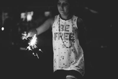 Young woman burning sparkler while standing outdoors at night