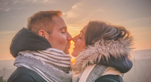 Close-up of couple kissing against sky during sunset
