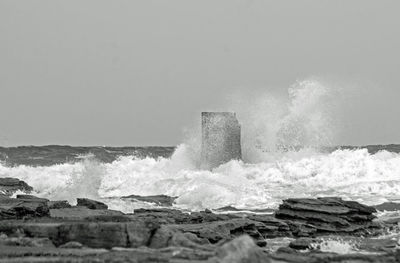 Waves breaking on rocks against clear sky