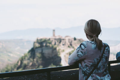 Rear view of woman standing by railing against sky