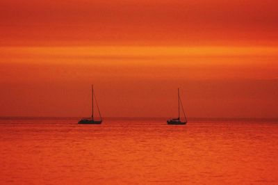 Silhouette boats sailing in sea against orange sky at sunset