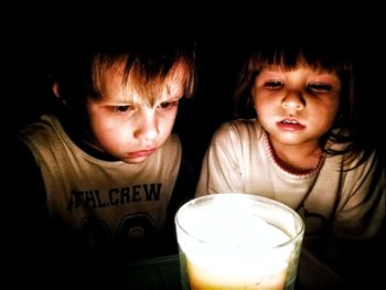 Close-up of siblings looking at lit tea light candle in darkroom