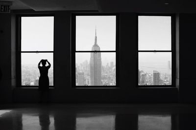 Rear view of silhouette woman standing by window against empire state building