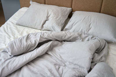 Crumpled bed with pillows, blanket and crumpled sheets in bedroom