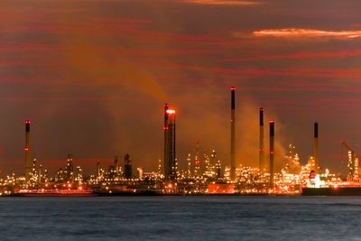 Low angle view of smoke emitting from industry by river against sky at keppel harbor