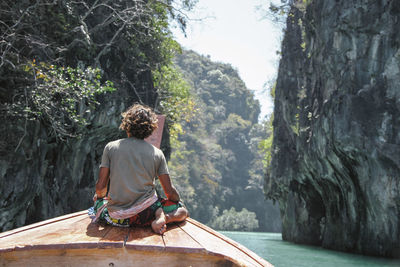 Rear view of man sitting on boat in sea amidst rock formations