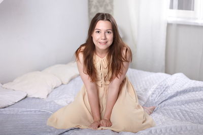 Portrait of smiling young woman sitting on bed at home