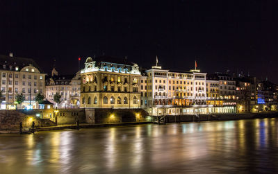 Illuminated buildings by river against sky at night