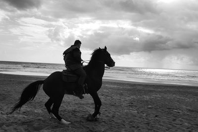 People on beach against cloudy sky