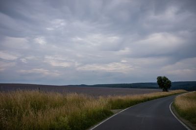 Empty road amidst field against sky