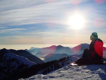 Person sitting on snowy field against mountains during sunset