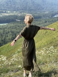 A young woman in a long dress fluttering in the wind stands on a mountainside in altai, russia.