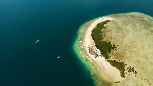 Tropical island and sandy beach with tourists surrounded by coral reef and blue sea in honda bay