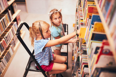 Schoolgirls looking for books in school library. students choosing set books. elementary education