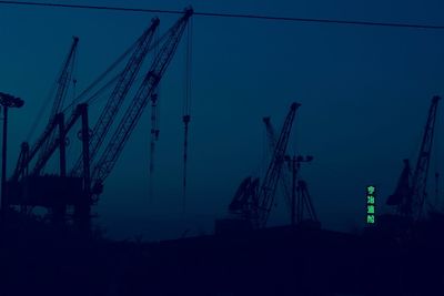 Low angle view of silhouette cranes against sky at dusk