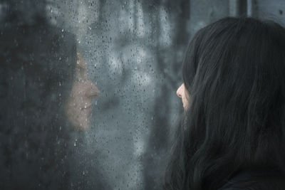 Close-up of wet woman looking through window