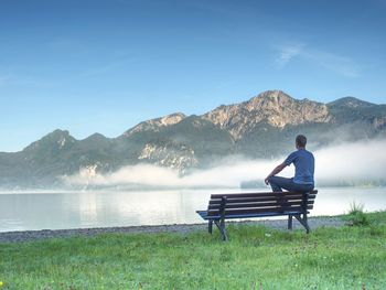 Man sit lone on a bench in park next lake. mountain range with amazing view over smooth lake 