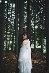 Woman standing by tree trunk in forest