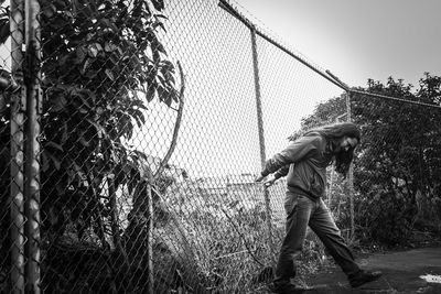 Rear view of boy looking through chainlink fence