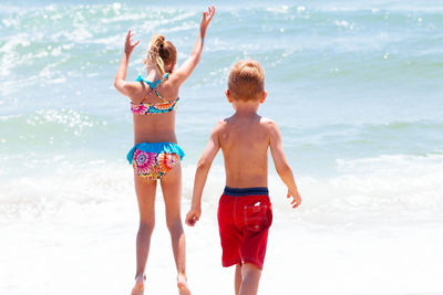 Rear view of siblings enjoying at beach during sunny day