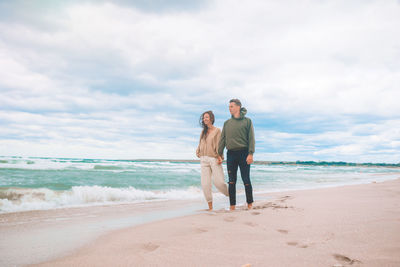 Full length of friends standing on beach against sky