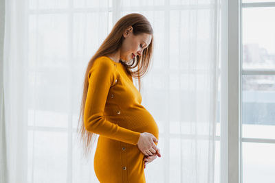 Young woman standing against window at home