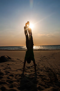 Silhouette woman standing at beach against sky during sunset