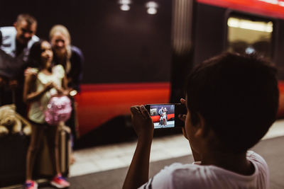 Boy photographing family on smart phone standing at railroad station platform