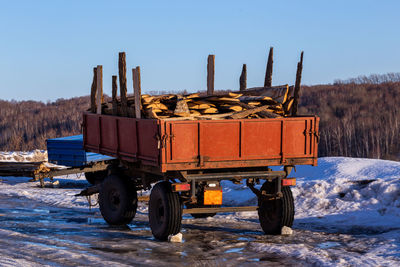 Old trailer filled with firewood on land against clear sky during winter