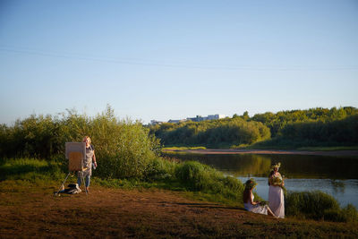 Rear view of woman standing by lake against clear sky