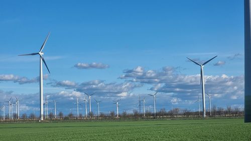 Wind turbines on field against blue sky