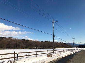 Road by electricity pylon against sky during winter