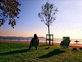 Rear view of man sitting on landscape against clear sky