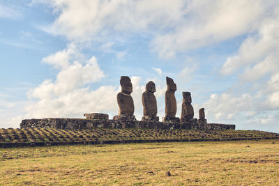 Low angle view of moai statues against cloudy sky